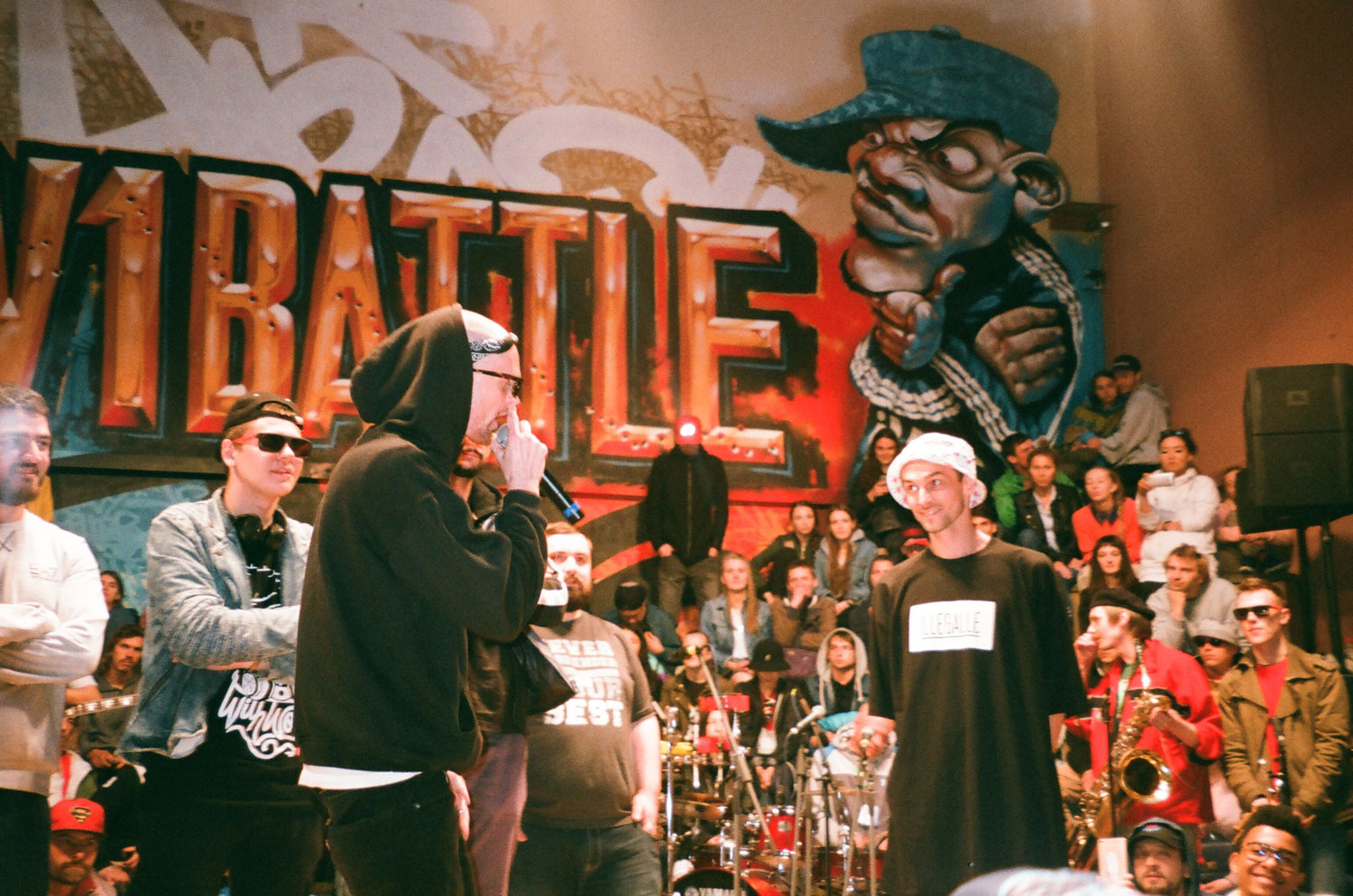 Rap battle with a crowd and a graffiti mural in the background